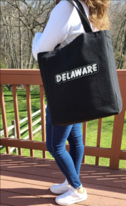 Woman holding black tote bag with "Delaware" on it on her left shoulder.